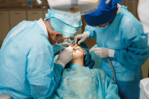 Two dentists perform oral surgery on a patient in a dental operatory.