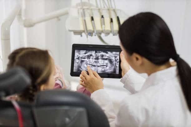 Pediatric dentist explains panoramic dental X-ray to child on a tablet
