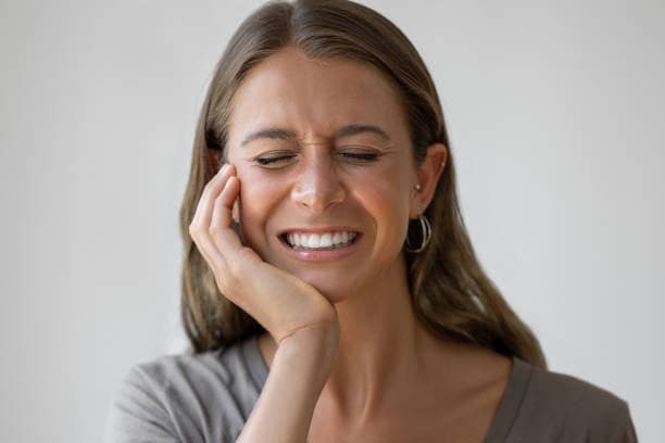 Person wincing, eyes closed, hand on cheek near jaw