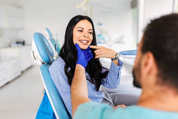 Dentist examines patient in dental chair as she points to her teeth