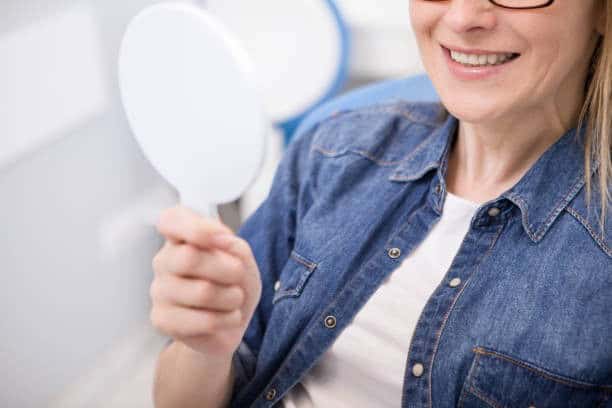 Paziente sorridente che controlla i denti con uno specchietto manuale sulla poltrona odontoiatrica.
