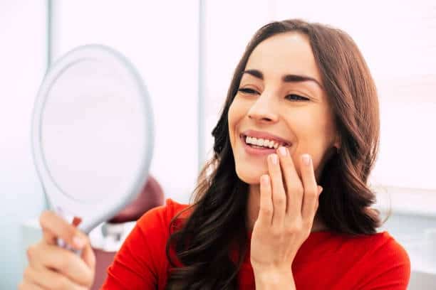 Woman smiling and checking her teeth with a handheld mirror at dental clinic.