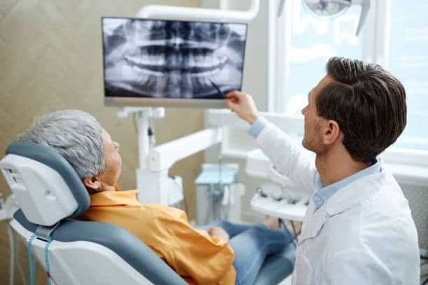 Dentist pointing to panoramic dental x-ray on monitor during patient consultation