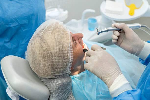 Dentist uses drill and mirror to treat patient in a dental chair.