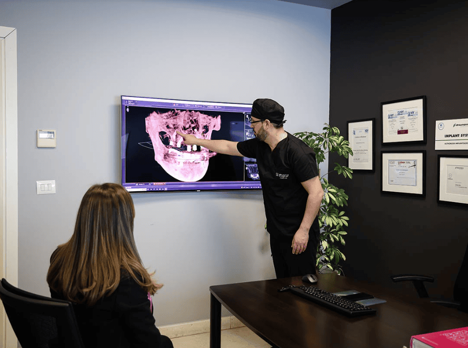 Dentist reviews 3D dental implant scan on screen with seated patient