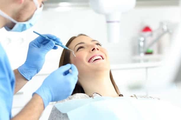 Dentist examines smiling patient with mirror and explorer in modern dental clinic.