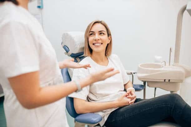 Smiling patient in dental chair speaking with dentist during treatment consultation.
