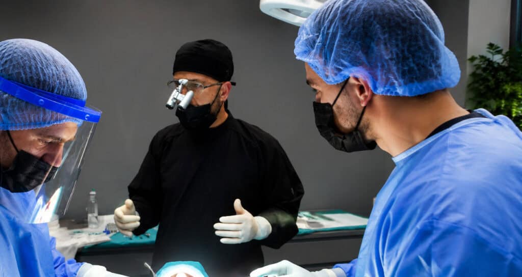 Dentisti me doreza të zeza përputh udhëzuesin e nuancave të dhëmbëve me dhëmbët e buzëqeshur të pacientit, konsultim për fasetat.