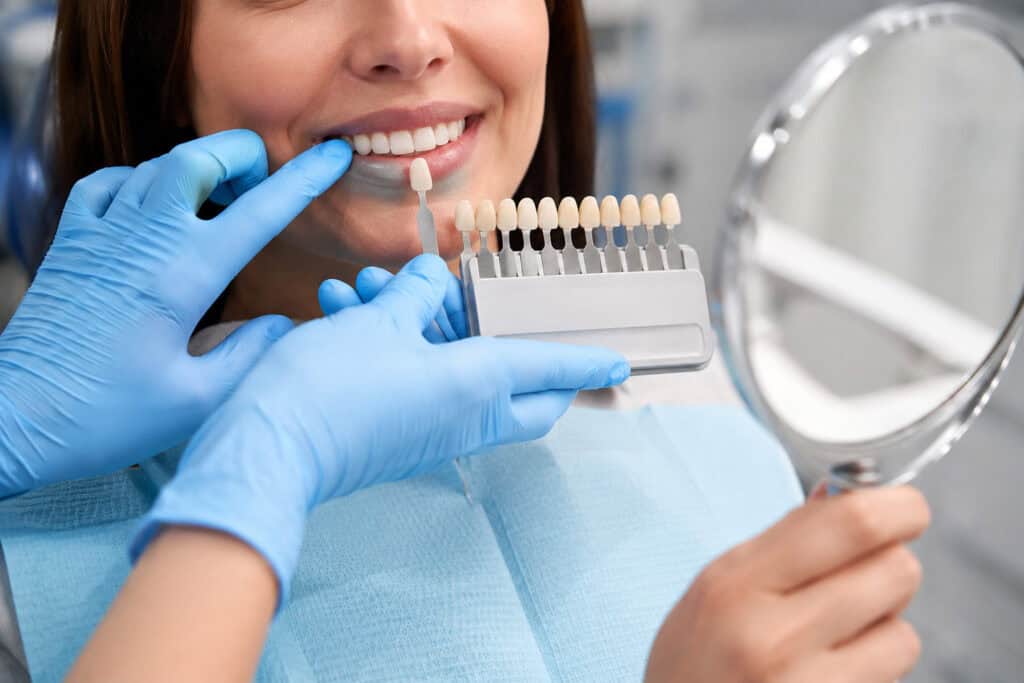 - Dentisti shpjegon implantet All-on-4 duke përdorur një model; pacienti buzëqesh pranë monitorit me skanimin 3D.- Konsultë për implante në një klinikë moderne, me panoramën e Tiranës të dukshme përmes dritareve nga dyshemeja në tavan.- Dentisti shqyrton me pacientin skanimet CT të implanteve full-arch; valixhja e kabinës sugjeron turizëm dentar.- Klinicisti me uniformë blu të errët tregon një model nofulle gjatë takimit për planifikimin e implanteve dentare.- Pacienti diskuton opsionet All-on-6 ndërsa paraqitjet 3D të implanteve shfaqen në ekranin pranë karriges.- Konsultë miqësore për implante dentare, me pamje të qytetit dhe një valixhe të vogël udhëtimi pranë.- Dentisti dhe pacienti janë ulur pranë monitorit që shfaq harqe me disa implante dentare.- Dhomë moderne trajtimi me radiografi të implanteve në ekran, pacienti buzëqesh gjatë konsultës.- Profesionisti dentar diskuton urën fikse full-arch, duke demonstruar modelin e dhëmbëve para një pacienti të vëmendshëm.- Konsultë në klinikën dentare në Tiranë, me imazhet e planifikimit të implanteve të shfaqura në monitor me rezolucion të lartë.