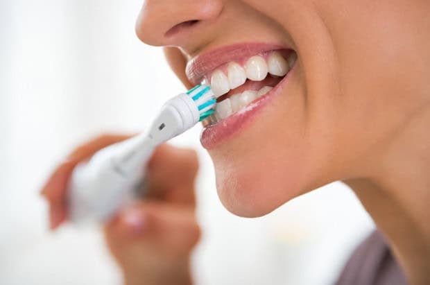 Close-up of person brushing teeth with electric toothbrush for oral hygiene, healthy gums.